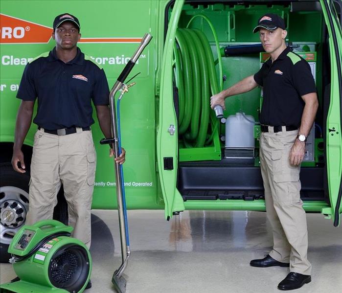 two men in uniforms holding drying equipment outside of a green SERVPRO van