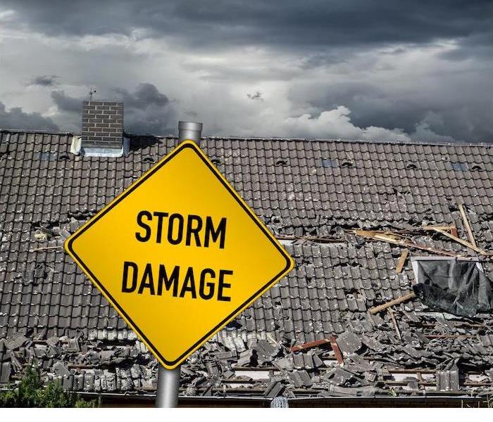 a yellow storm damage sign in front of a large damaged roof